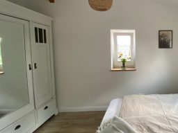 Storchennest Schlafzimmer Schlafzimmer mit Bett, weißem Kleiderschrank und Fenster mit Blumen.