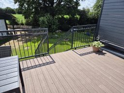 Balkon mit Holzboden und blühendem Topfpflanze, Blick auf grüne Wiese.