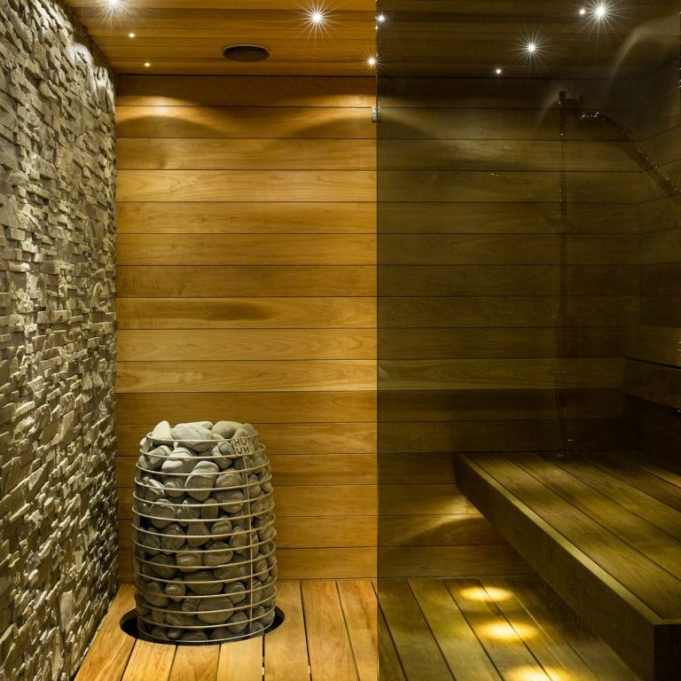 Sauna Moderne Sauna mit Holzverkleidung, Steinbrunnen und gedämpfter Beleuchtung.
