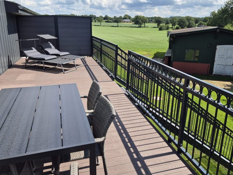 Storchennest Balkon Terrasse mit Tisch und Stühlen, Blick auf einen grünen Rasen und eine Gartenhütte.