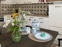 Storchennest Küche Tischgedeck mit blumigem Arrangement, Teekanne und Tellern in einer modernen Küche.